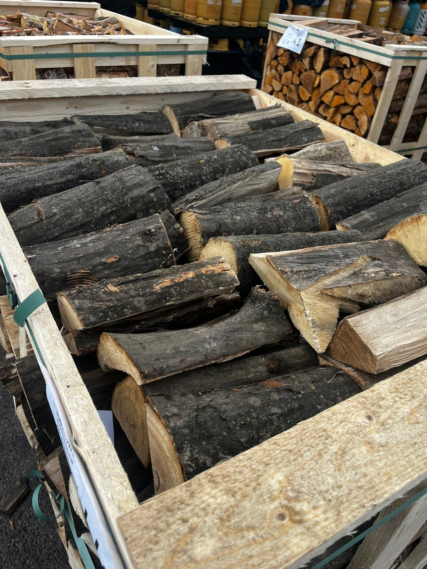 Stacks of firewood in wooden crates with a background of stacked logs. Murphys Direct UK